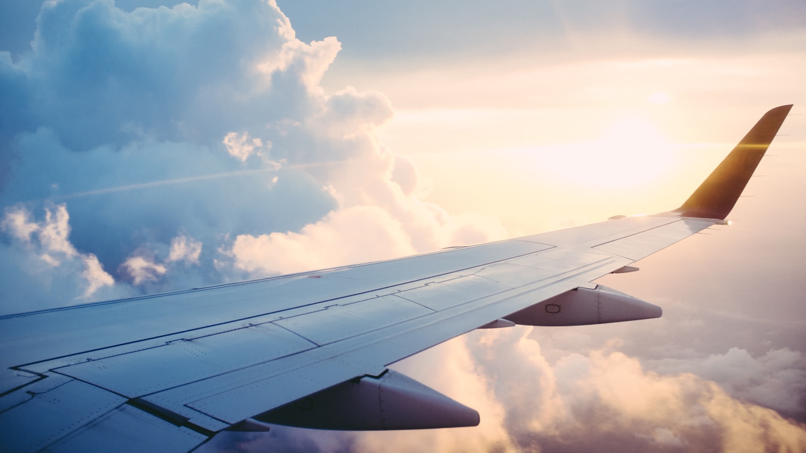 An airplane wing seen through the cabin window above a layer of bright clouds.
