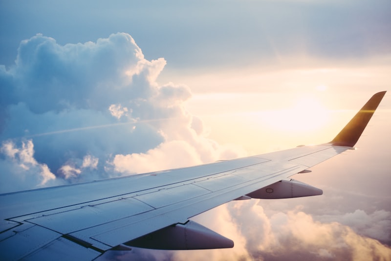 An airplane wing seen through the cabin window above a layer of bright clouds.