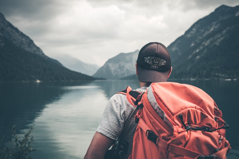 A traveller sitting on a wooden dock looking out over calm water with a small backpack beside them.