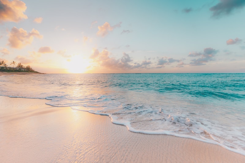 A traveller standing on a quiet beach at sunset with calm water stretching out ahead.